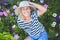 Happy smiling elderly senior woman having fun posing in summer garden with flowers in straw hat. Farming, gardening, agriculture,