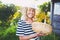 Happy smiling elderly senior woman in straw hat having fun posing in summer garden with flowers in basket. Farming, gardening,