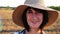 Happy smiling female farmer looks into camera standing at wheat field. Portrait of adult beautiful agronomist with straw