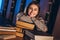 Happy smiling female student has completed the exam preparation. The girl leaned on a stack of books sitting in the library at