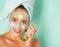 Happy smiling fresh looking young woman with a towel at her head and clay mud musk with cucumber do spa procedures