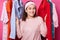 Happy smiling girl stands between hangers with blouses in fashion store. Cheerful woman visits boutique. Cute lady likes to go to
