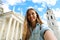 Happy smiling girl taking selfie picture in front of Vilnius Cathedral, Lithuania. Beautiful young woman traveling in Europe