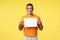 Happy smiling hispanic male in orange t-shirt, holding paper over chest and grinning as give advice, write favorite