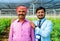 Happy smiling indian supportive banker with Indian farmer standing at green house by looking at camera - concept of