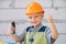 Happy smiling kid boy twists bolt with screwdriver. Child repairman with repair tool. Child in helmet and boilersuit on