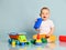 Happy smiling laughing infant baby boy toddler in yellow pants and white t-shirt is sitting surrounded by toys, playing