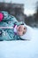 Happy and smiling little child lying on snow and looking at camera, winter season with slippery surface