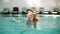 Happy smiling little kid is swimming together with his mother in the swimming pool. Young mother is spinning and