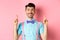 Happy smiling man in bow-tie pointing, looking up, showing something cool, standing on pink background