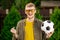 Happy smiling man in everyday clothes posing with soccer ball on green backdrop