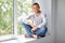 Happy smiling man sitting on window sill in lotus pose