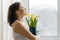 Happy smiling mature woman with bouquet of yellow flowers standing at home near the window, spring season