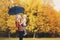 Happy smiling mother holding child with umbrella having fun together over autumn trees