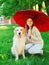 Happy smiling owner and Golden Retriever dog together hiding under umbrella on grass in summer