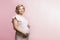 Happy smiling pregnant blonde woman stands and touches big belly. Waiting for the birth of a baby. Pink background. Space for text