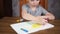 A happy smiling preschooler boy sits at a table and draws with bright pencils on paper. Development and education of