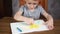 A happy smiling preschooler boy sits at a table and draws with bright pencils on paper. Development and education of