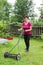 Happy smiling senior woman mowing grass with lawn mower in the garden