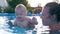 Happy smiling toddler doing splashes in pool, mother and child together have fun in summer
