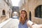 Happy smiling traveler girl taking selfie in the Street of the Knights of Rhodes city, Greece. Young female traveler visiting