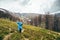 Happy smiling traveller senior beautiful woman in blue rain jacket and jeans in mountains surrounded by forest, enjoying