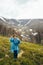 Happy smiling traveller senior beautiful woman in blue rain jacket and jeans in mountains surrounded by forest, enjoying