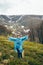 Happy smiling traveller senior beautiful woman in blue rain jacket and jeans in mountains surrounded by forest, enjoying silence