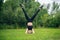 Happy smiling woman enjoy gymnastic yoga doing headstand asana on a forest meadow.