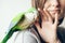 Happy smiling woman is gently touching lovely domesticated parrot. Close-up of friendly and cute Monk Parakeet. Green Quaker is