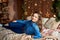Happy smiling woman in jeans clothing lying on bed with garland on wood wall at home bedroom, copy space. Cozy home moment.