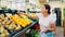 Happy smiling woman making purchases in supermarket, choosing fresh ripe tangerines