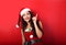 Happy smiling woman in santa claus clothing showing and advertising the finger on something empty above the head on red background