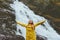 Happy smiling woman tourist raised hands enjoying waterfall