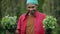 Happy smiling young African American man holding flowers for transplanting in hands standing in garden. Portrait of