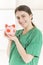 Happy smiling young beautiful female doctor with stethoscope holding pink piggy bank