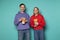 Happy smiling young couple in casual clothes standing against blue wall with popcorn in hands