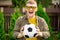 Happy smiling young man posing with soccer ball on green lawn of country house