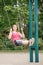 Happy smiling young middle age woman girl in red tshirt and jeans shorts on swing on backyard playground