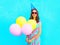 Happy smiling young woman in a birthday cap with an air colorful balloons over a blue