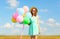 Happy smiling young woman holds an air colorful balloons enjoying a summer day on a meadow blue sky
