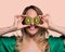 Happy and smiling young woman playing with a cut of Kiwi fruit in half and in front of her eyes. Photo on solid color background