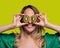 Happy and smiling young woman playing with a cut of Kiwi fruit in half and in front of her eyes. Photo on solid color background