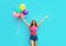 Happy smiling young woman raising her hands up with bunch of balloons having fun wearing a shorts and pink t-shirt on blue wall