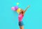 Happy smiling young woman raising her hands up with bunch of balloons having fun wearing a shorts and pink t-shirt on blue wall