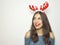 Happy smiling young woman with reindeer horns on her head looks your product on white background. Copy space.