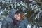 Happy snow covered couple kissing under fir branches in winter forest. Concept healthy romantic holidays on fresh air
