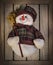 Happy snowman plush toy with a broom and dressed warm, over wooden texture background