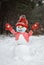 happy snowman in red knitted hat  sweater  mittens  medical mask with smile painted on it stands in snowy forest