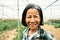 Happy southeast Asian woman smiling at the camera while working inside agricultural greenhouse